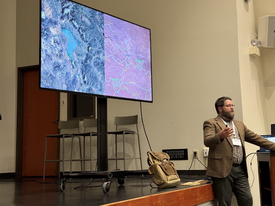 Nate Loper Presenting Grand Canyon Geology Research Nate Loper speaking at a conference with Grand Canyon maps displayed on a large screen